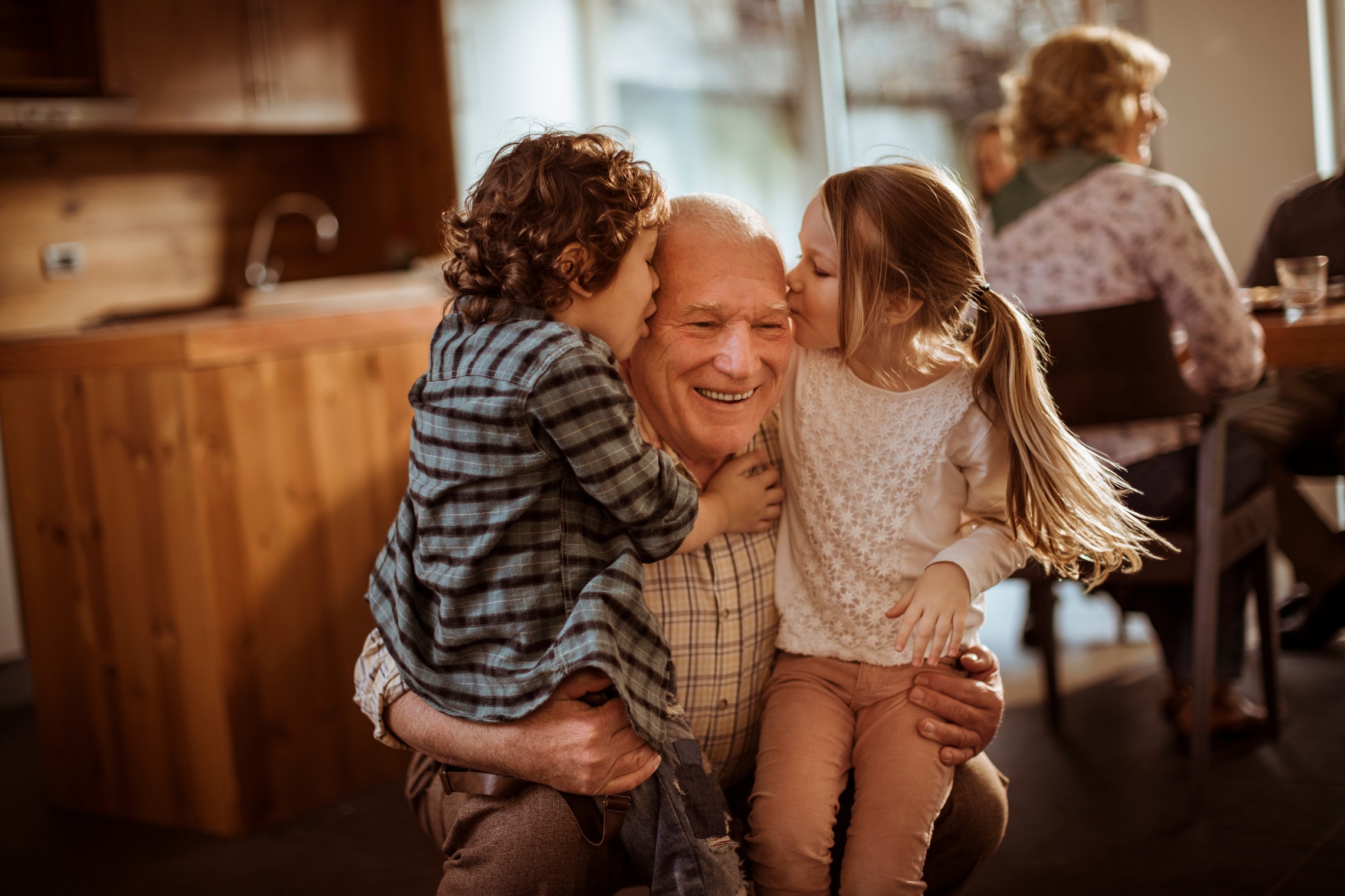 Vorsorge treffen: Das Bild zeigt einen Großvater, der von seinen Enkelkindern einen Kuss bekommt.