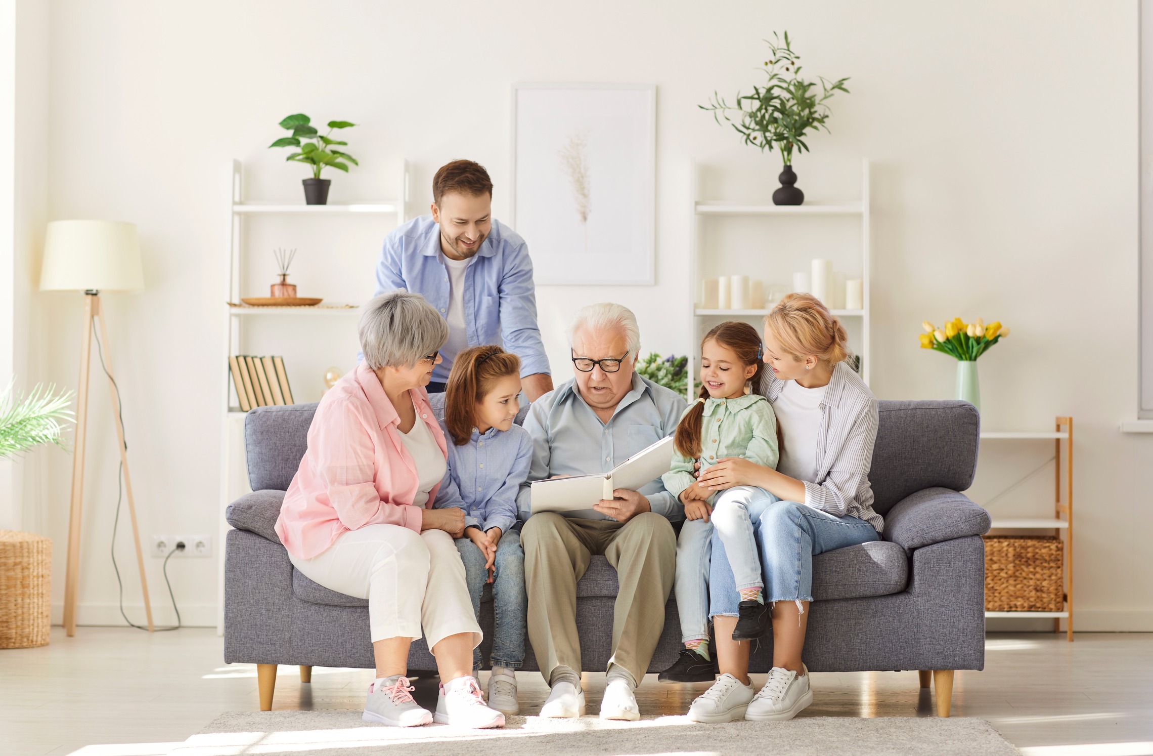 Ein Großvater, der auf dem Sofa sitzt und mit seinen Kindern und Enkelkindern ein Buch anschaut. 