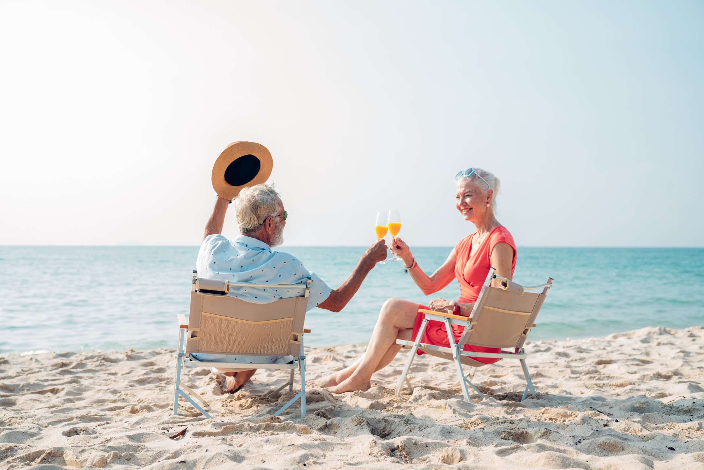 Sicherheit für Ihre Zukunft Das Bild zeigt einen älterer Mann und eine ältere Frau, die in Liegestühlen am Strand sitzen und anstoßen.